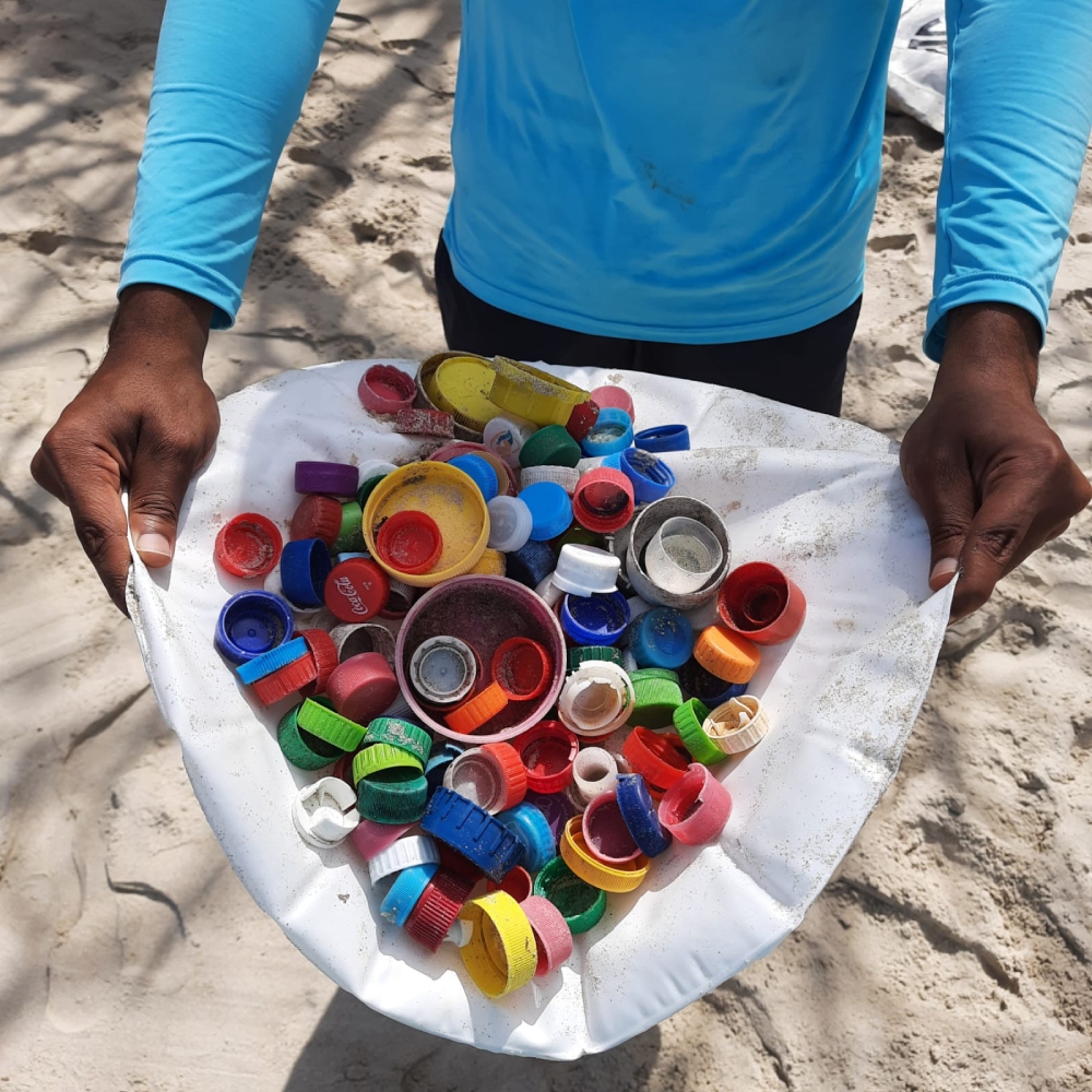 Homem segurando várias tampinhas de plástico recolhidos do oceano
